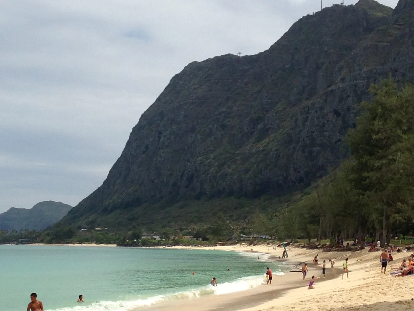 Beachgoers along the shore at Waimānalo Beach Park with mountains behind